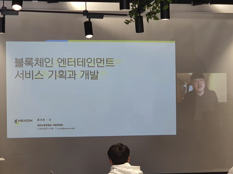 비대면 강연 현장 사진. 스크린에 '블록체인 엔터테인먼트 서비스 기획과 개발'이라는 발표 표지가 띄워져 있고, 오른쪽 작은 창에 화상으로 연결된 내 얼굴이 보인다. 앞쪽에는 청중의 뒷모습이 있다.